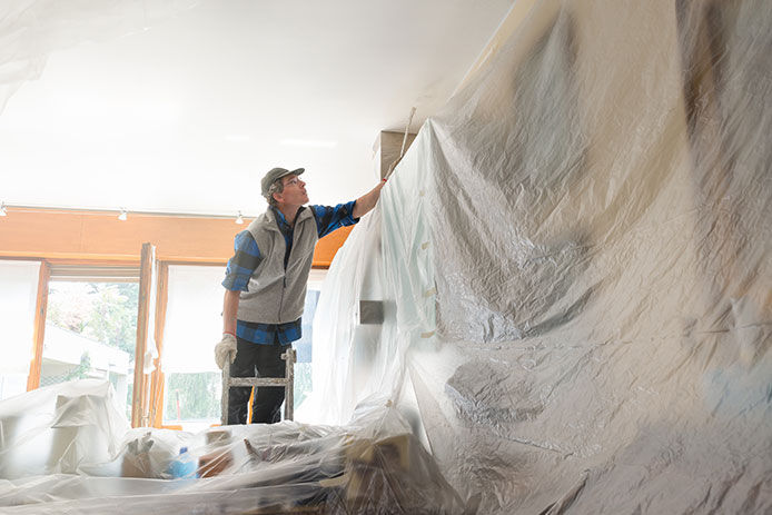 A man covering a living room in plastic