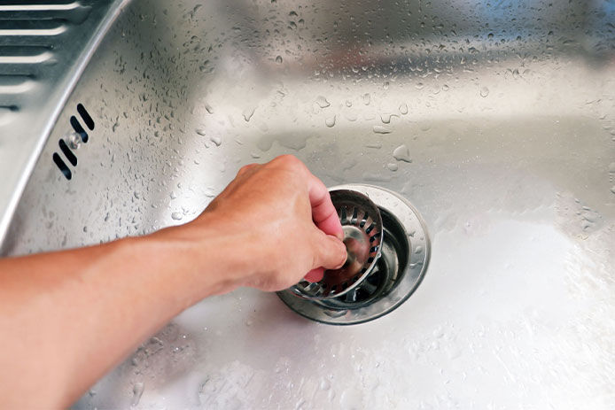 Person placing a sink stopper in kitchen sink drain to prevent clogs