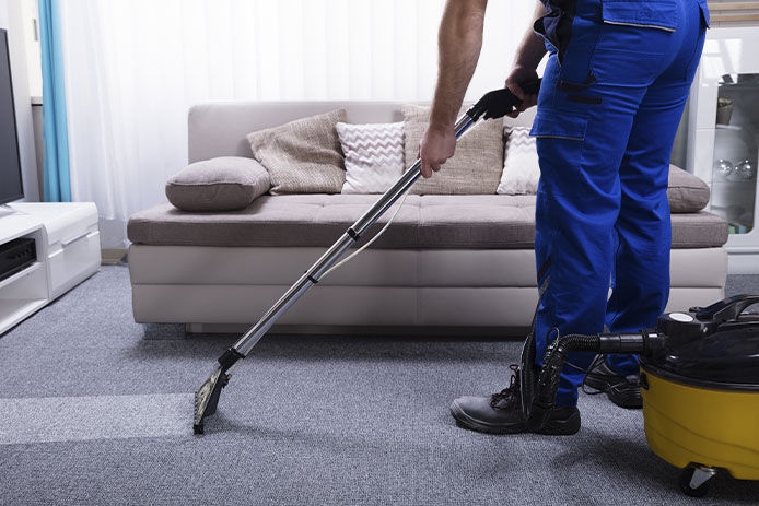 A professional cleaner vacuuming the carpet in a living room next to a couch