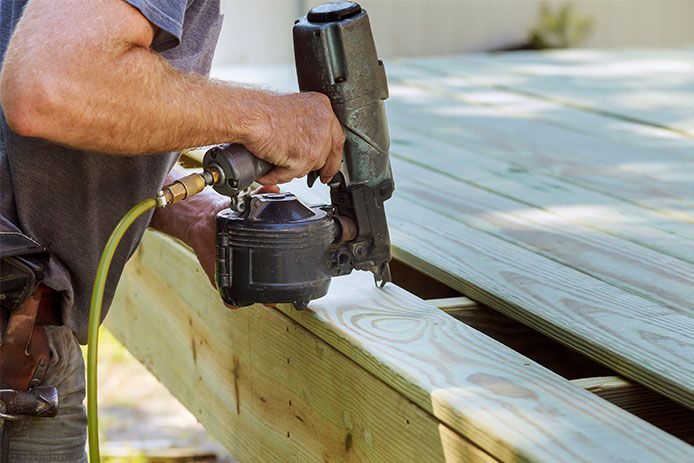 Man using a nail gun connected to a compressor to build a deck