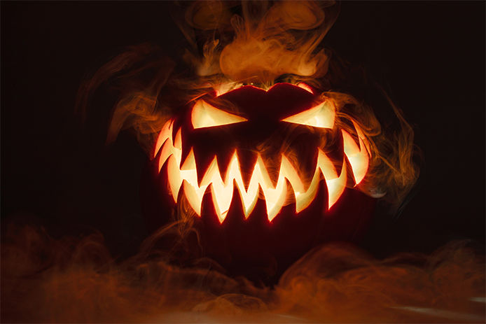 Fuming bright Jack-o'-lantern pumpkin on dark solid background. Glowing eyes and a terrible grin. Halloween minimal concept