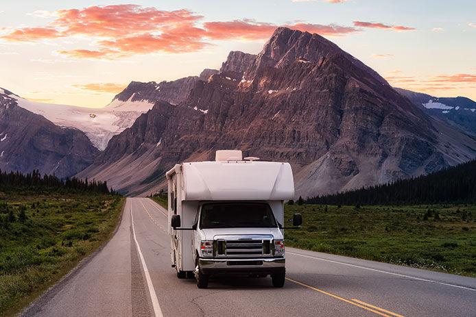 A RV on the road driving away with beautiful sky and mountains in the background