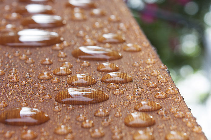 Summer rain on cottage deck: A lengthwise view of water droplets repelling on a wooden deck rail after a summer rain shower, with selective focus.