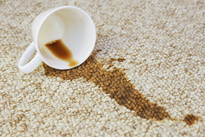 White mug laying on tan carpet with coffee spilt on the floor