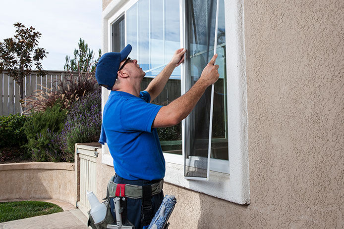 Man removing window screen from the outside of house