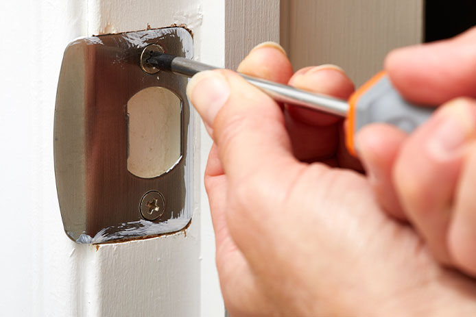 A person screwing in a strike plate on a door way