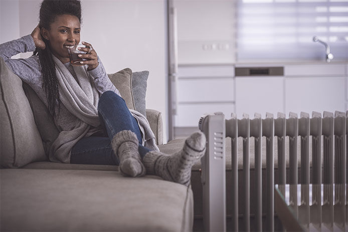 A woman relaxing on a couch with a space heater next to her