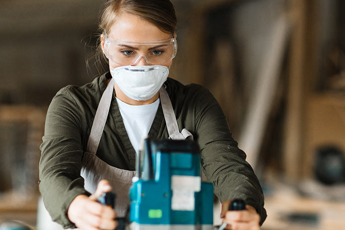 A woman wearinf safety googles and a mask while using a router