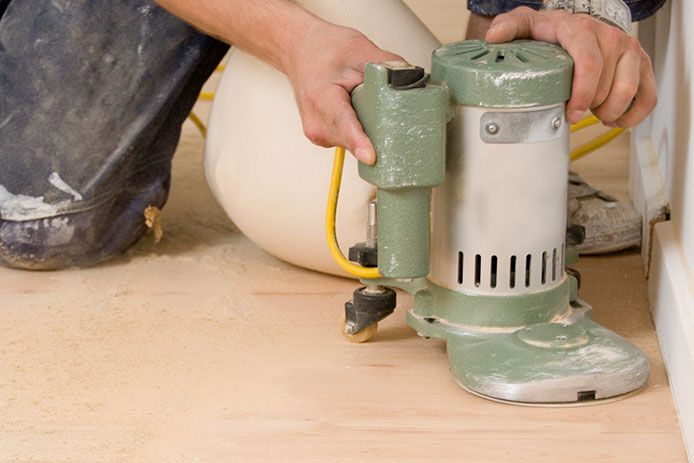 Person sanding down the old finish on wood floor