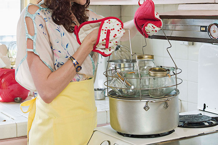 Woman with hot pads on her hands putting canning jars into a pot of boiling water