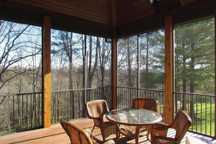 A wooden screened in back porch with patio furniture