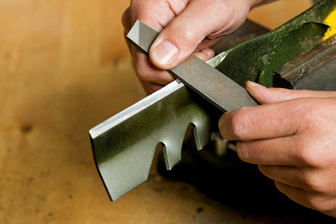 Person sharpening mower blade on a workbench, close-up