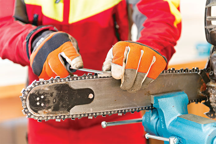 Person wearing work gloves while sharpening the chain blades on the chainsaw