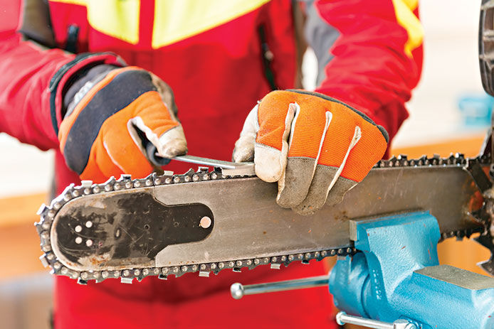 Person wearing safety gloves while working on the chain of a chainsaw