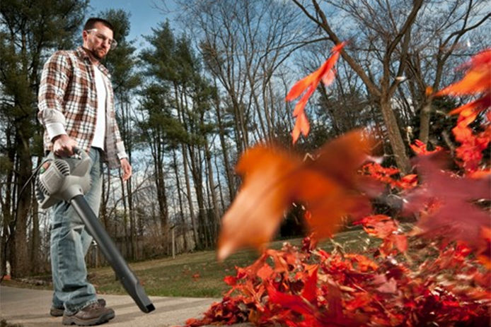 A man using his blower vacuum to clean up leaves outside