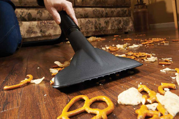 A close up image of a wet/dry vacuum cleaning up a bunch of pretzels and other snacks on the ground