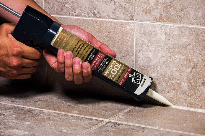close up of a caulking gun on a tiled surface. The caulking gun has silicone caulking, great for home improvement projects.