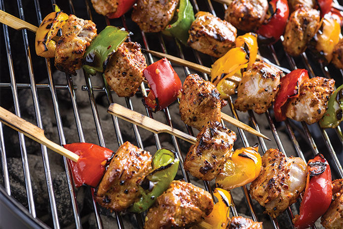 Chicken and peppers skewers sitting on top of a charcoal grill grate