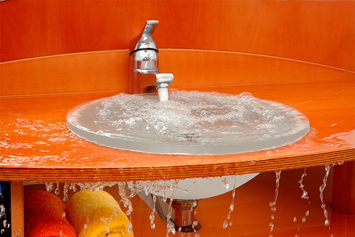 An orange bathroom countertop with an overflowing bathroom sink. 