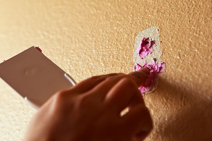 Person filling in a small hole with joint compound using their finger