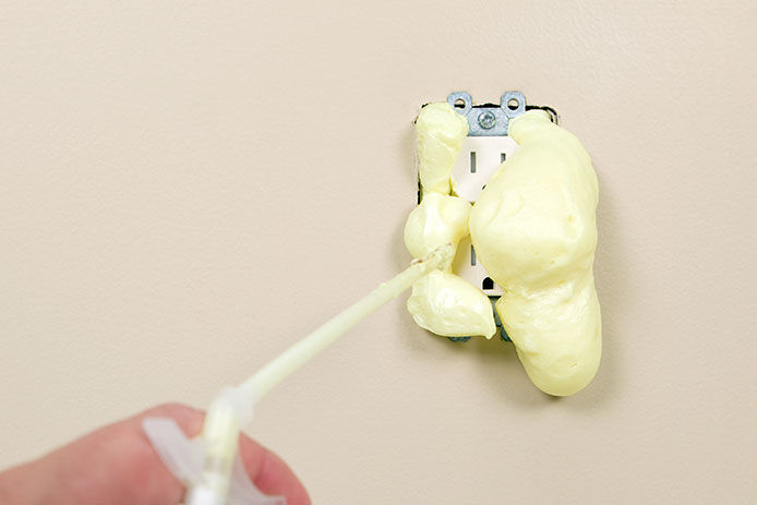 Over using spray foam on an electrical plug. The foam is pushing out from behind the electrical outlet encasing the plugs