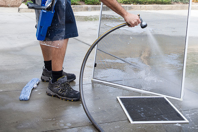 Man spraying soap suds off of window screen with a hose