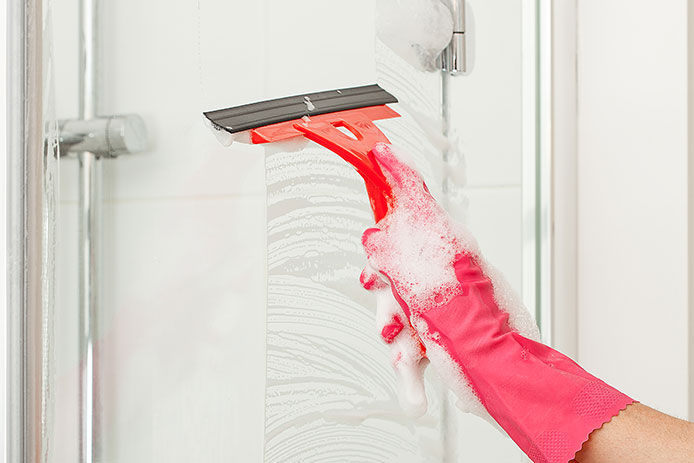A person squeegeeing a shower door