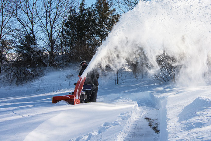 A man dressed in black using a snow blower plowing snow after snow storm in the morning