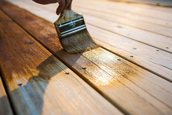 Male Carpenter Applying Varnish To Wooden Deck