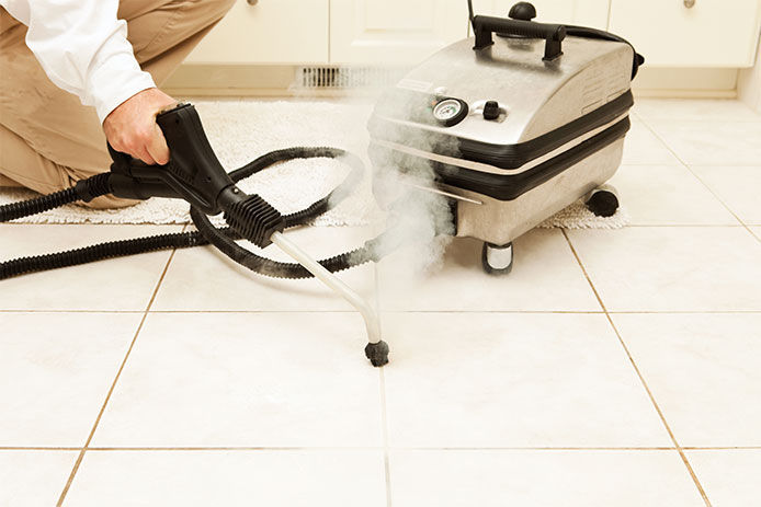 A man using a steam cleaner to clean grout in a kitchen 