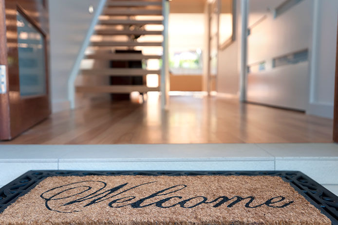 Focus on the front doormat looking into an open front door and hallway with wood floors