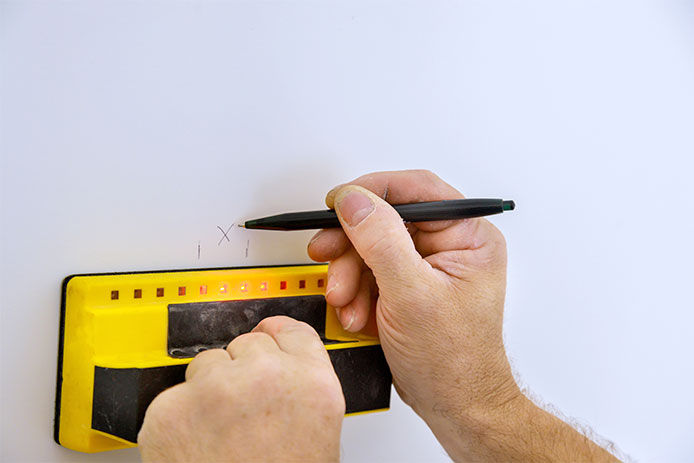 Man using a stud finder to mark it with a pen on white wall