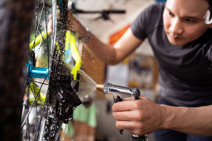 A young male mechanic cleaning the spokes and chain on a bicycle.