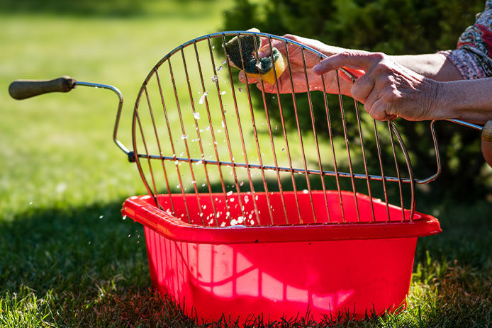 A grill is getting cleaned by a woman after a barbecue with a sponge.