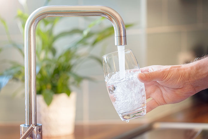 Hand holding a glass filling it up with water from the kitchen sink faucent