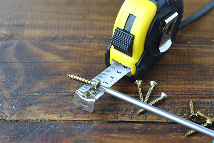 A tape measure, screws, and screwdriver on a wood table