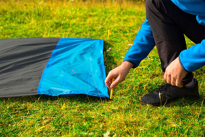 A man placinga. tarp into a lawn using plastic stakes