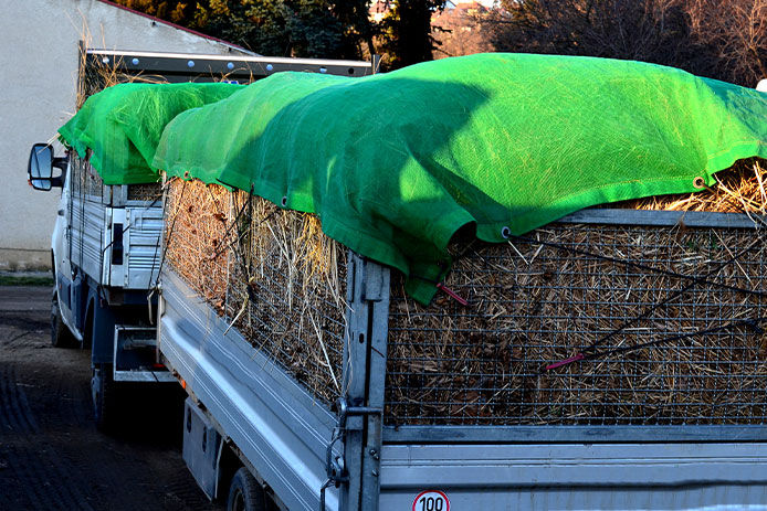 A truck with a trailer filled with grass clippings is covered with two green tarps to hold in the debris