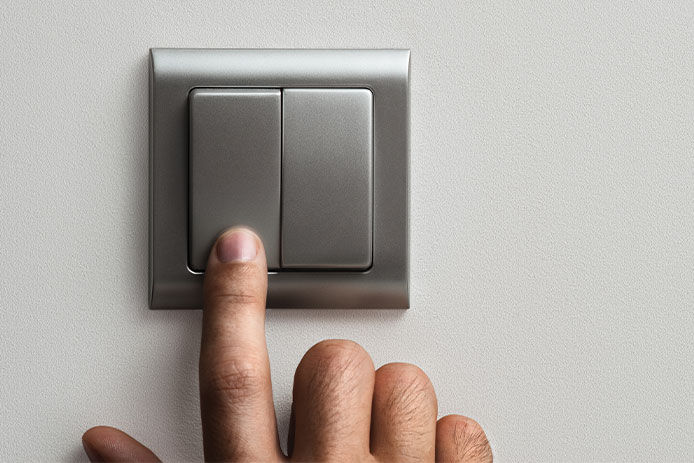 A person presses a brushed silver dual light switch with their pointer finger.