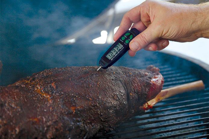 A thermometer stucked inside a pork brisket on a charcoal grill.