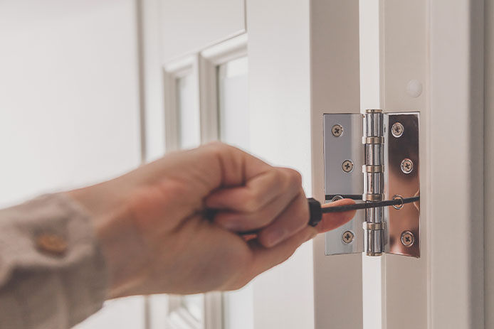 A person tightening the hinges on a door