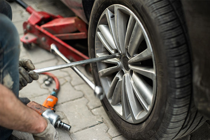 Man using a lug wrench to take lug nuts off of a tire