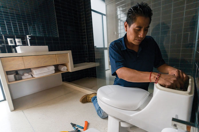 Latin American plumber fixing a toilet in the bathroom