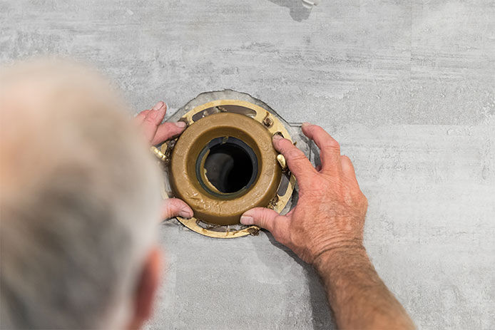 A senior man installing a toilet wax ring on a concrete floor 