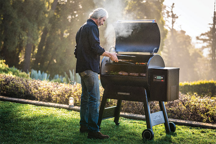 Older man using a Treager pellet grill to cook dinner outside 