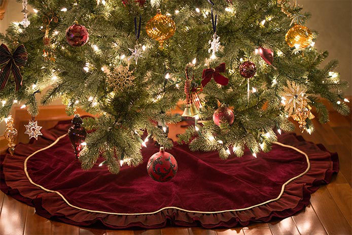 a maroon traditional tree skirt underneith a lite Christmas tree