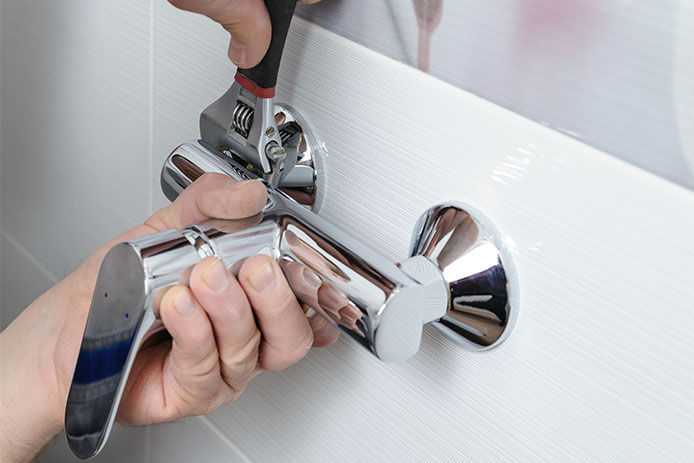 A person tightening a bath tub faucet