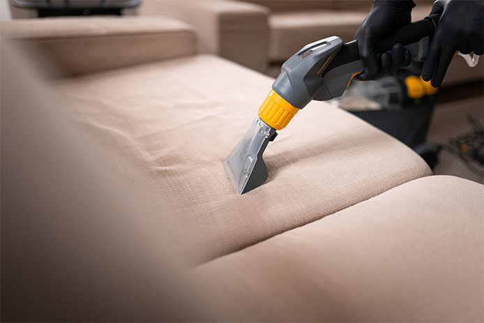 A handheld upholstery cleaner cleaning a beige couch in a residential living room