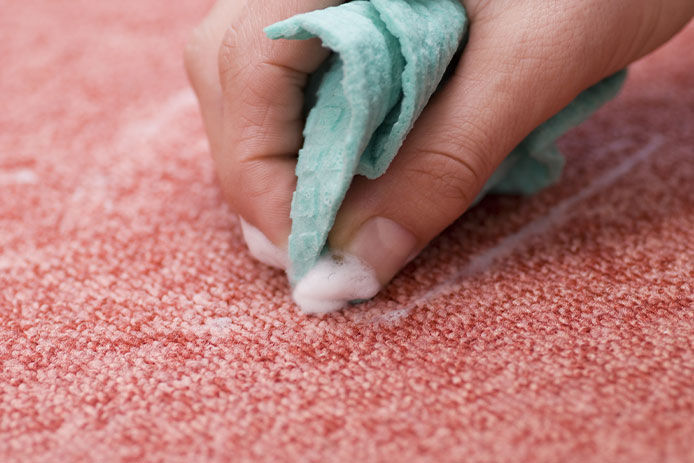 Spot cleaning a spot in pink carpet with a teal microfiber cloth