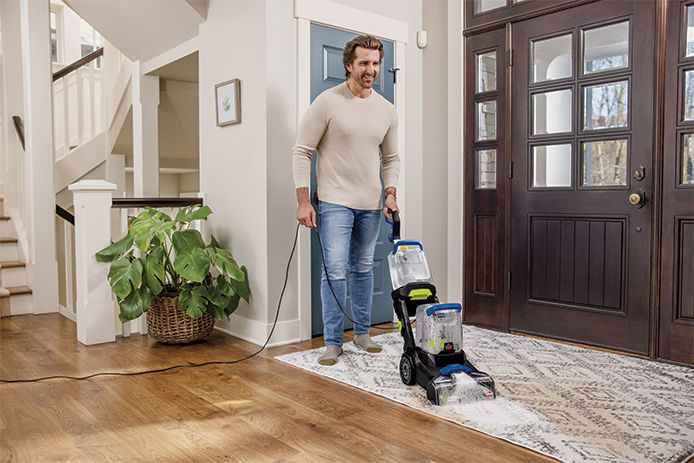 An average man using a carpet cleaner to clean the entry rug of his house 